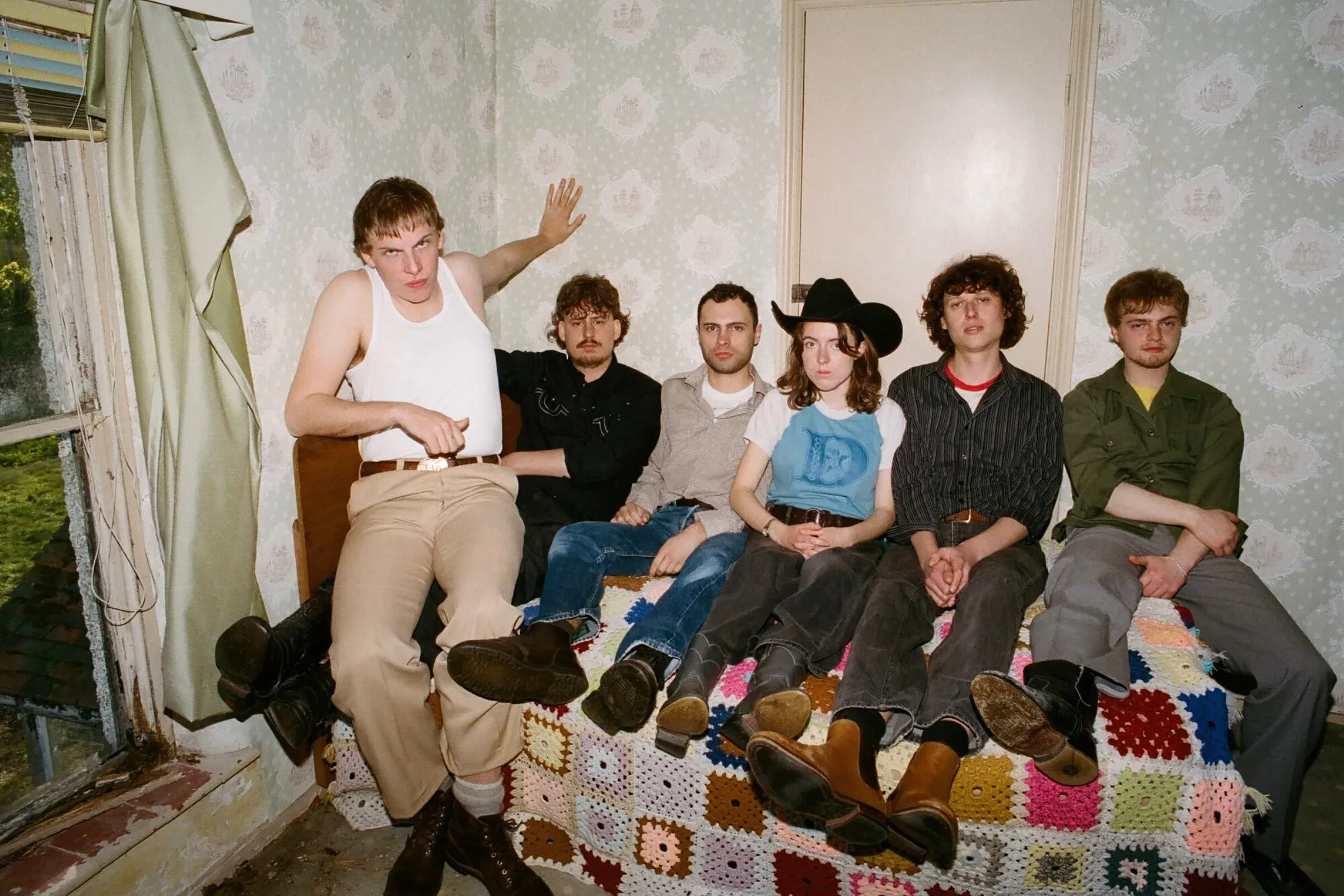 The members of Fat Dog sit together in a worn, wallpapered room, photographed by Emma Toma.